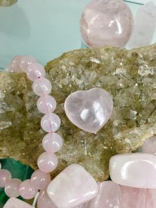 A rose quartz bracelet with a rose quartz heart laying on top of cluster of lithium quartz